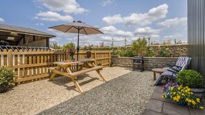 Un espace patio aménagé avec une table et un banc en bois, un parasol et un barbecue.