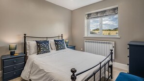 Une chambre à coucher comprenant un lit, des tables de chevet, une commode, une fenêtre donnant sur un paysage agréable et un radiateur.