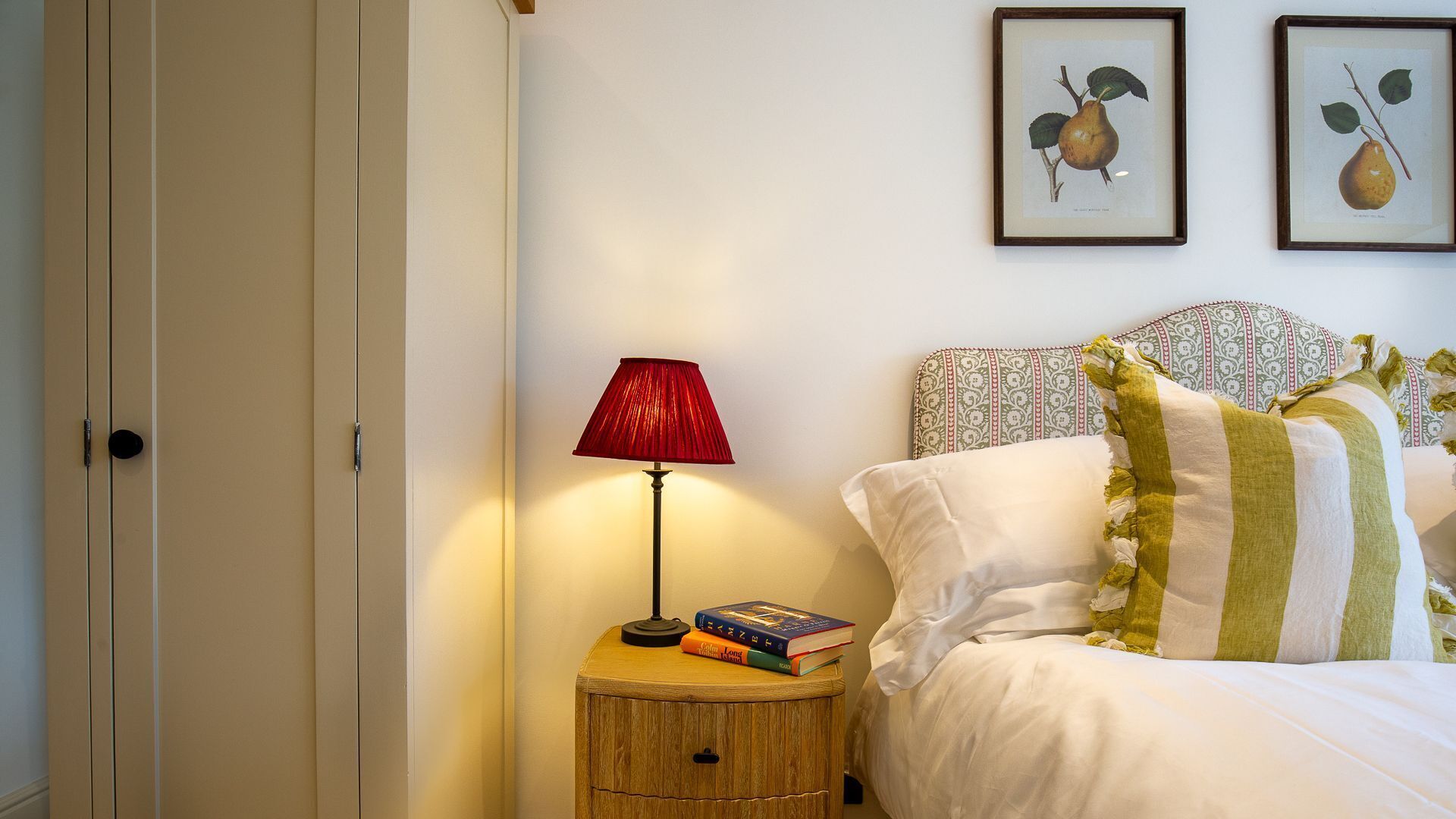 Une chambre à coucher avec un lit, une table de chevet avec une lampe, et deux reproductions botaniques encadrées accrochées au mur.