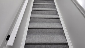Una scala con gradini rivestiti di moquette e corrimano bianchi, che porta a un pianerottolo.