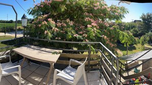 Eine Terrasse mit Tisch und Stühlen, Blick auf einen Garten mit blühenden Bäumen und ein entferntes Feld.