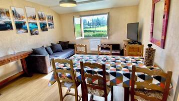 A dining area with a large table, wooden chairs, a sofa, and a TV.