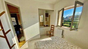 Ein Schlafzimmer mit Bett, Stuhl, Fenster und Spiegel.