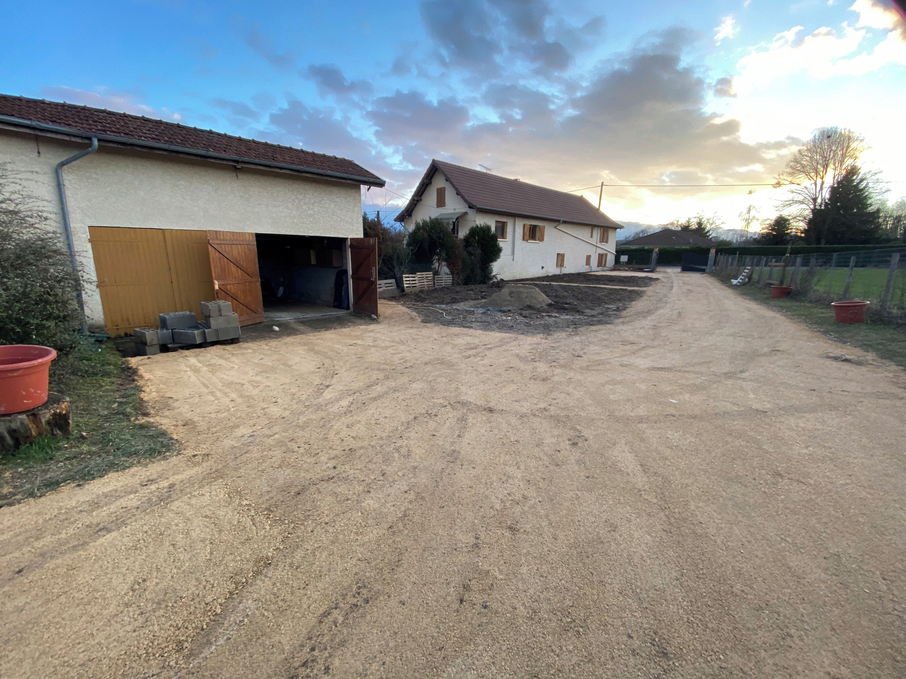 Une propriété située en zone rurale, avec une allée en gravier menant à un bâtiment blanc doté d’un garage.