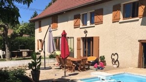 Ein zweistöckiges Haus mit rotem Ziegeldach, einem Swimmingpool und Gartenmöbeln, darunter ein Tisch und Stühle.