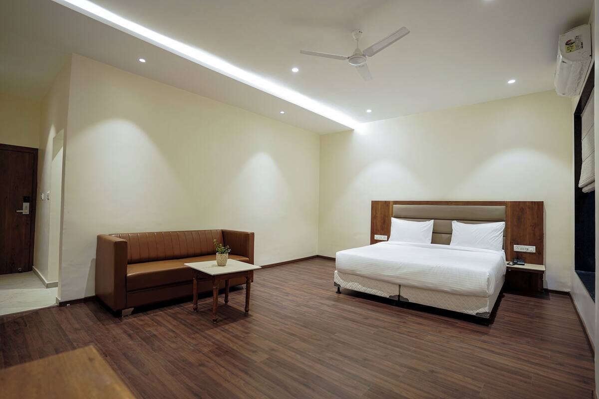 A hotel room with a bed, a sofa, a small table, and a ceiling fan.