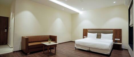 A hotel room with a bed, a sofa, a small table, and a ceiling fan.