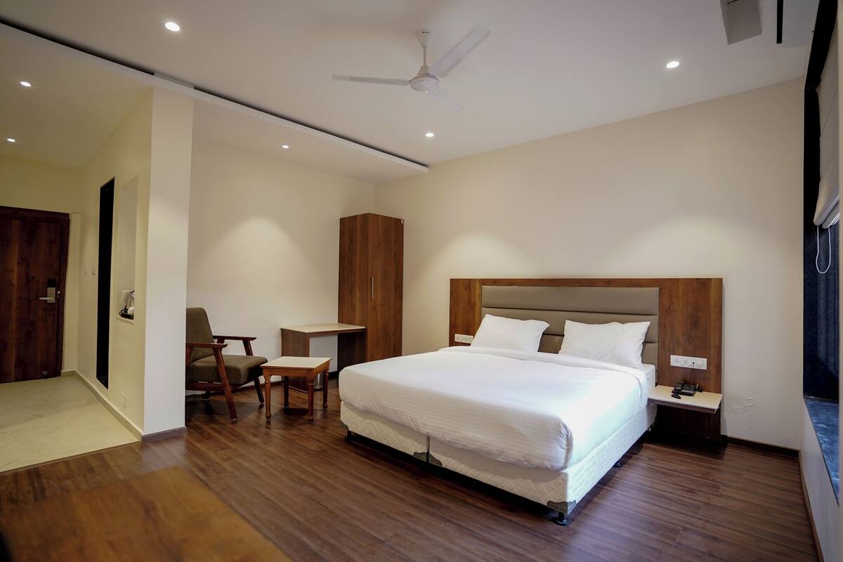 A modern hotel room with a large bed, wooden headboard, a desk, and a chair.