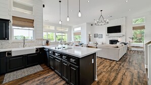 A spacious kitchen with a large island, dark cabinetry, and pendant lighting. - Luxurious Retreat on Lake LBJ: Pool, Hot Tub, Dock (Granite Shoals)