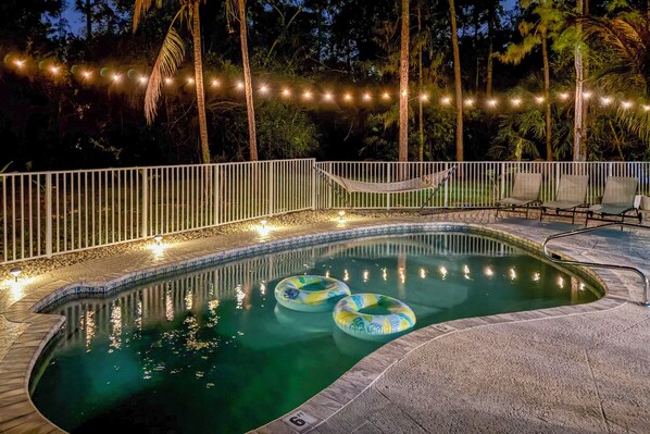 Una piscina con valla blanca, dos sillas de descanso y una hamaca.