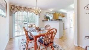 Un comedor con mesa y sillas de madera, una araña y vista a la cocina.