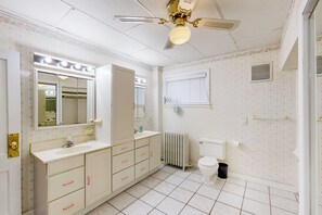 Un baño con tocador, espejo, inodoro, radiador y ventilador de techo.