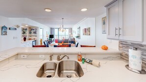 Een moderne keuken met een dubbele spoelbak, een marmeren aanrechtblad en uitzicht op de eethoek.