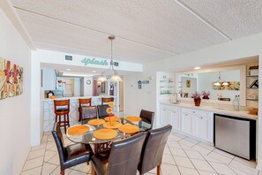 A modern kitchen with white cabinets, a dining area with a glass table and leather chairs, and a central island with a sink. - Coastal 2BR, Steps to Gulf: Suntide III - Unit 709 (South Padre Island)