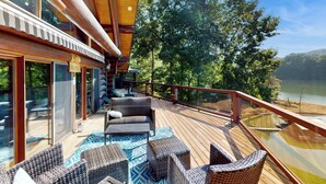 Une terrasse en bois, meublée de meubles en osier, et une porte vitrée donnant sur une pièce.