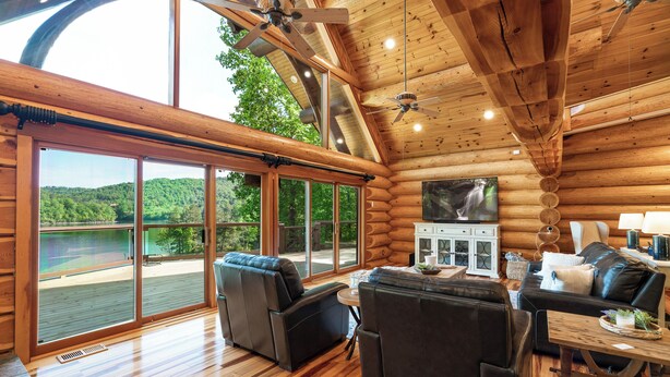 Un intérieur spacieux de chalet en bois, avec une grande porte-fenêtre coulissante donnant sur une terrasse qui offre une vue sur un lac.