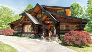 Une cabane en rondins avec des fondations en pierre, un porche à l’avant avec des marches et une allée menant à l’entrée.