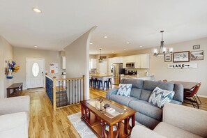 A spacious living room with a grey sofa, wooden coffee table, and a kitchen in the background. - Fun on the Cove! Home w/ Dock & Foosball (Climax Springs)