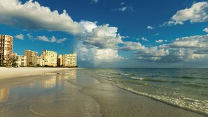 A beachfront hotel with multiple high-rise buildings, a sandy beach, and a clear blue sky with clouds. - Swim Spa + Dock! Boater's Retreat on Marco Island (Marco Island)