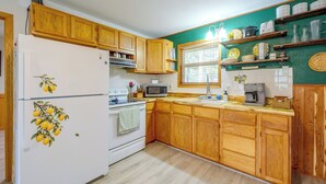 Una cocina con gabinetes de madera, un refrigerador blanco, una estufa, un microondas y una cafetera.