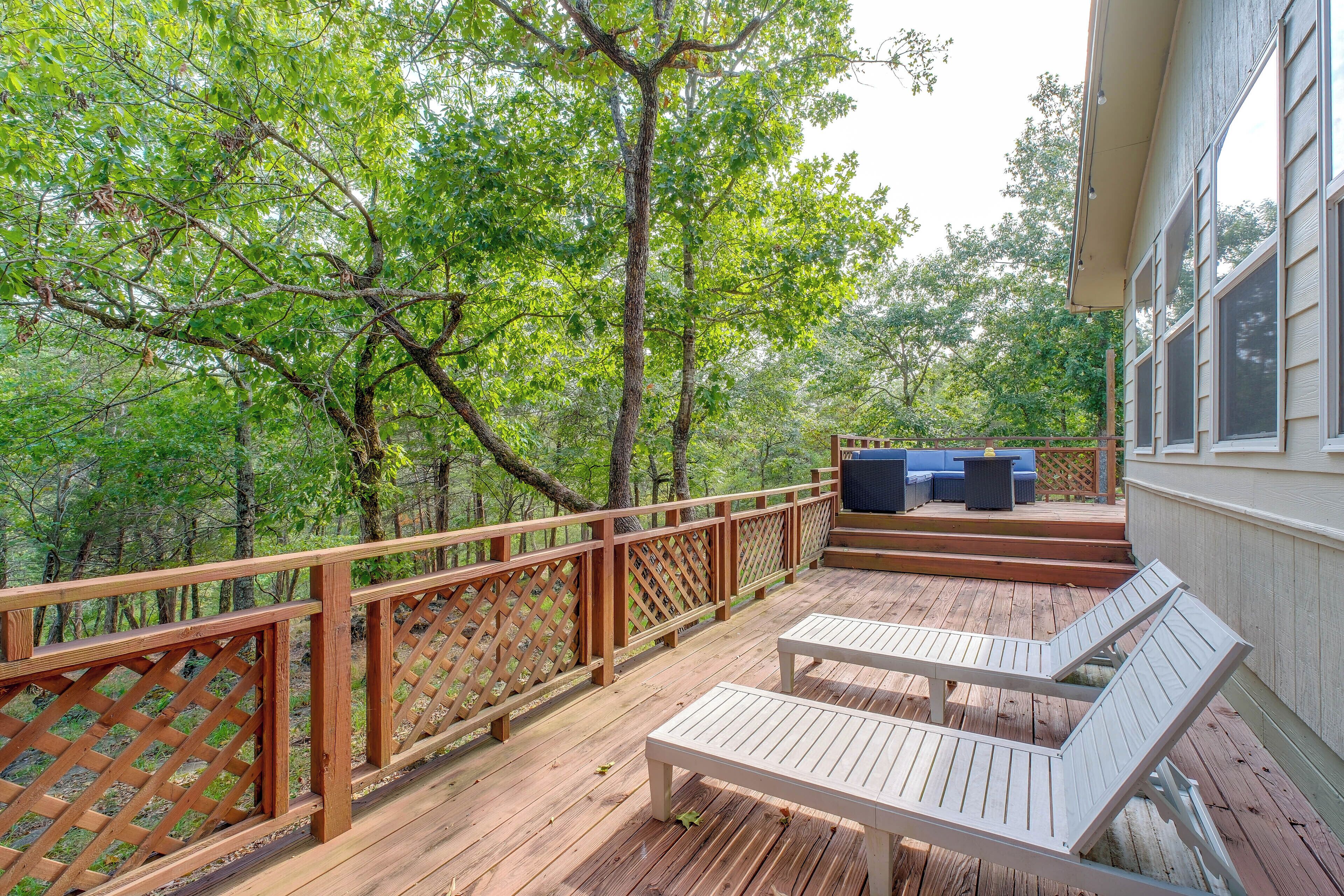 A wooden deck with a white bench and a blue sofa, surrounded by trees.