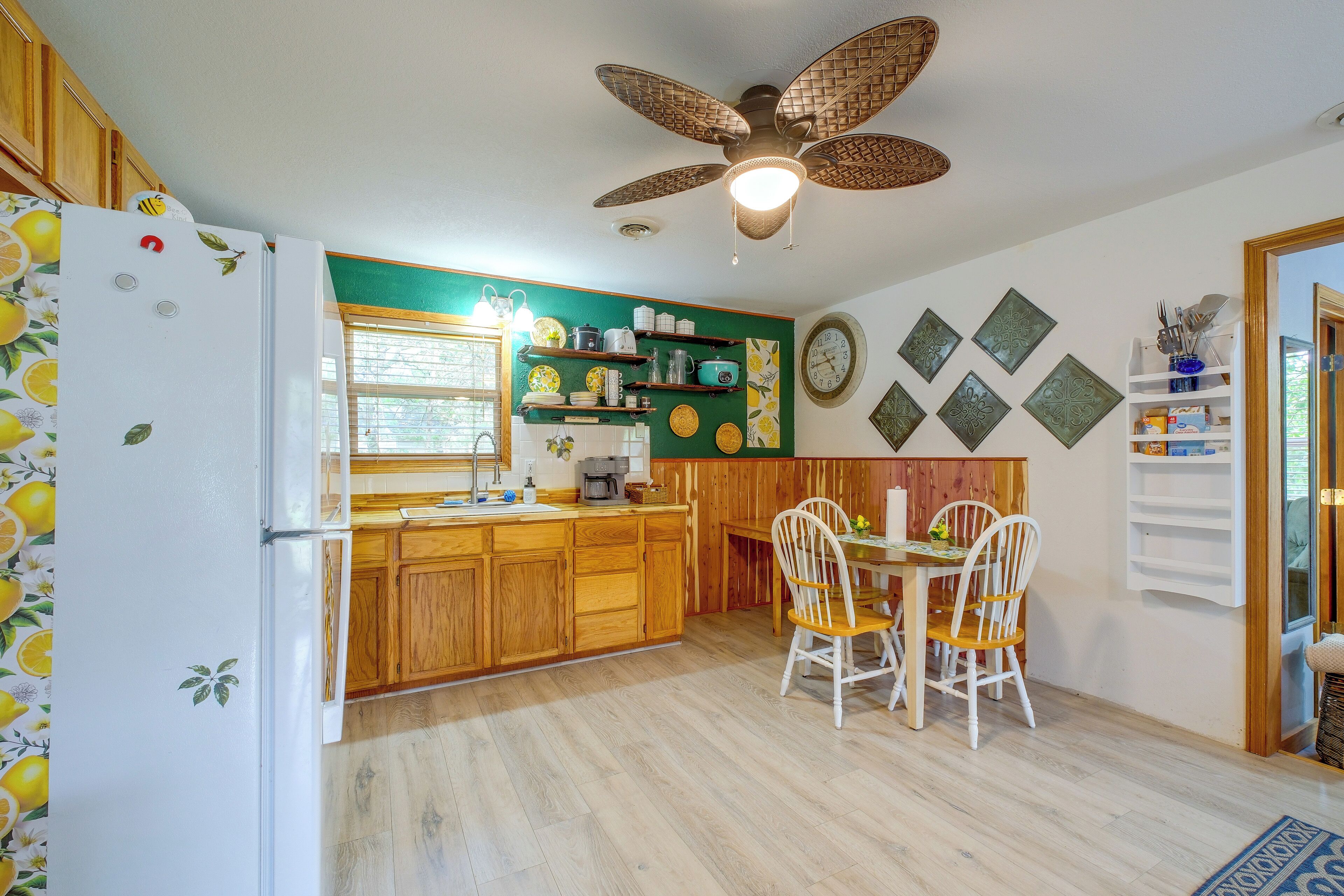 A kitchen with wooden cabinets, a dining table with chairs, a ceiling fan, and decorative wall plates.