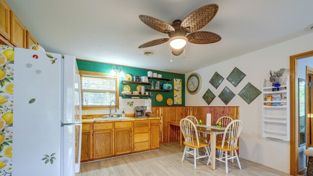 Une cuisine avec des meubles de rangement en bois, une table à manger avec des chaises, un ventilateur de plafond et des décorations murales.