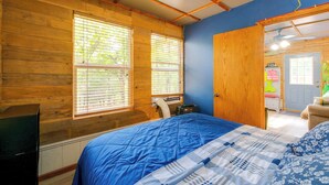 Une chambre avec des murs en bois, une couvre-lit bleue et une fenêtre avec des stores.