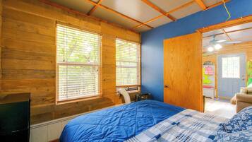 A bedroom with wooden walls, a blue bedspread, and a window with blinds.