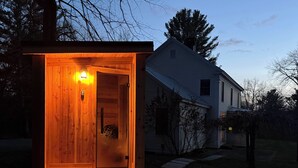A wooden cabin with a lit interior, a door, and a small porch area. - Close to Copake Lake! 4-Season Escape w/ Sauna (Copake)
