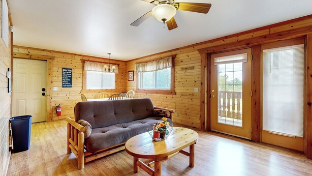 A cozy cabin interior with a wooden floor, a sofa, a dining table, and a ceiling fan. - Adventure Basecamp! Three Bears Resort Retreat (Warrens)