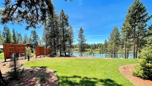 A well-maintained lawn with a wooden structure, surrounded by tall trees and a lake. - Angler's Oasis! Group-Friendly Deschutes River Gem (Bend)