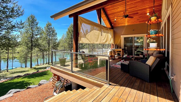 A wooden deck with outdoor furniture, a glass railing, and a view of a lake surrounded by trees. - Angler's Oasis! Group-Friendly Deschutes River Gem (Bend)
