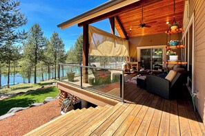 A wooden deck with outdoor furniture, a glass railing, and a view of a lake surrounded by trees. - Angler's Oasis! Group-Friendly Deschutes River Gem (Bend)
