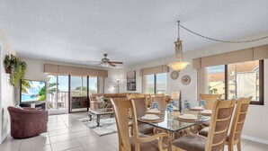 Ein geräumiges Wohnzimmer mit einem Glastisch, Holzstühlen und einem Deckenventilator.