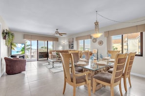 A spacious living room with a glass dining table, wooden chairs, and a ceiling fan.