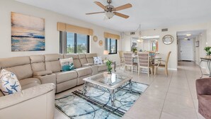 Ein geräumiges Wohnzimmer mit einem beigen Sofa, einem Glastisch und einem Deckenventilator.