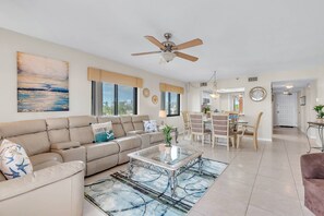 A spacious living room with a beige sofa, a glass coffee table, and a ceiling fan.
