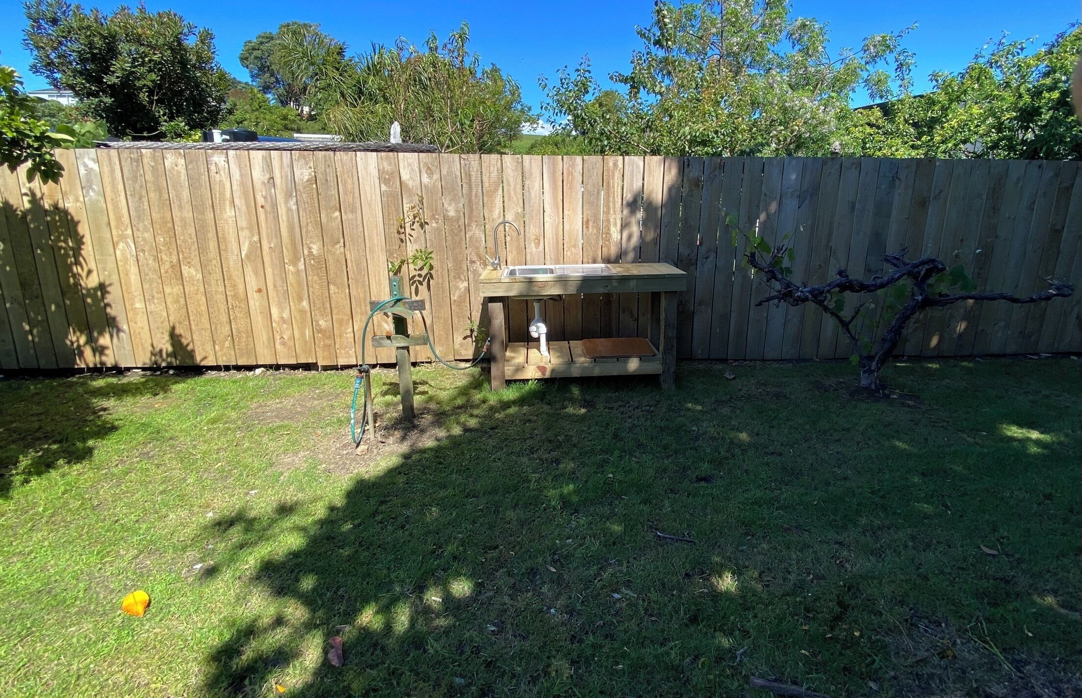 Une clôture en bois, une petite table avec un évier et un tuyau d’arrosage.