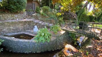 Un bassin en pierre, un pont en bois et une petite construction en bois dans un jardin.