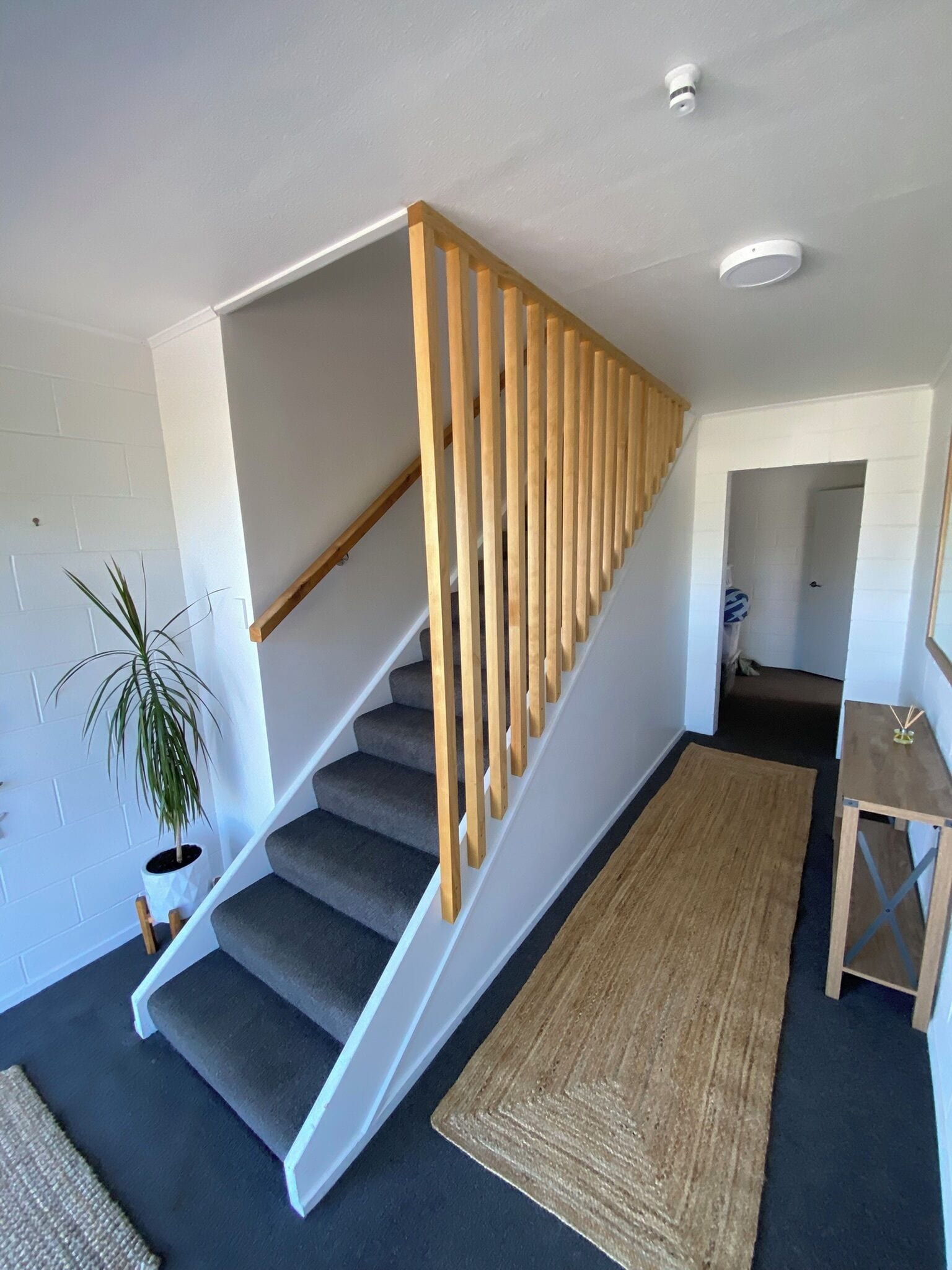 A staircase with wooden handrails, carpeted steps, and a small table with a plant.