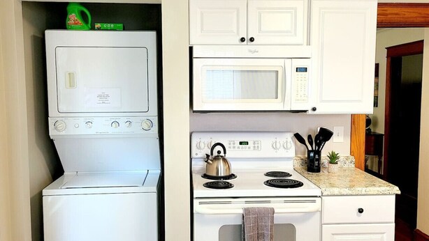 A compact kitchen with a washer-dryer unit, a microwave, and a stove. - Quiet Downtown Apt w/ Fireplace (Waterville)