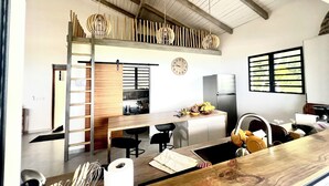 A modern kitchen with a wooden countertop, a built-in oven, and a refrigerator. There is a wooden ladder leading to a lofted dining area with a view of the kitchen.