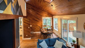A spacious living area with wooden flooring, a blue sofa, a dining table with chairs, and a large skylight.