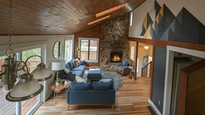 A cozy living room with a stone fireplace, wooden ceiling, and blue furniture.