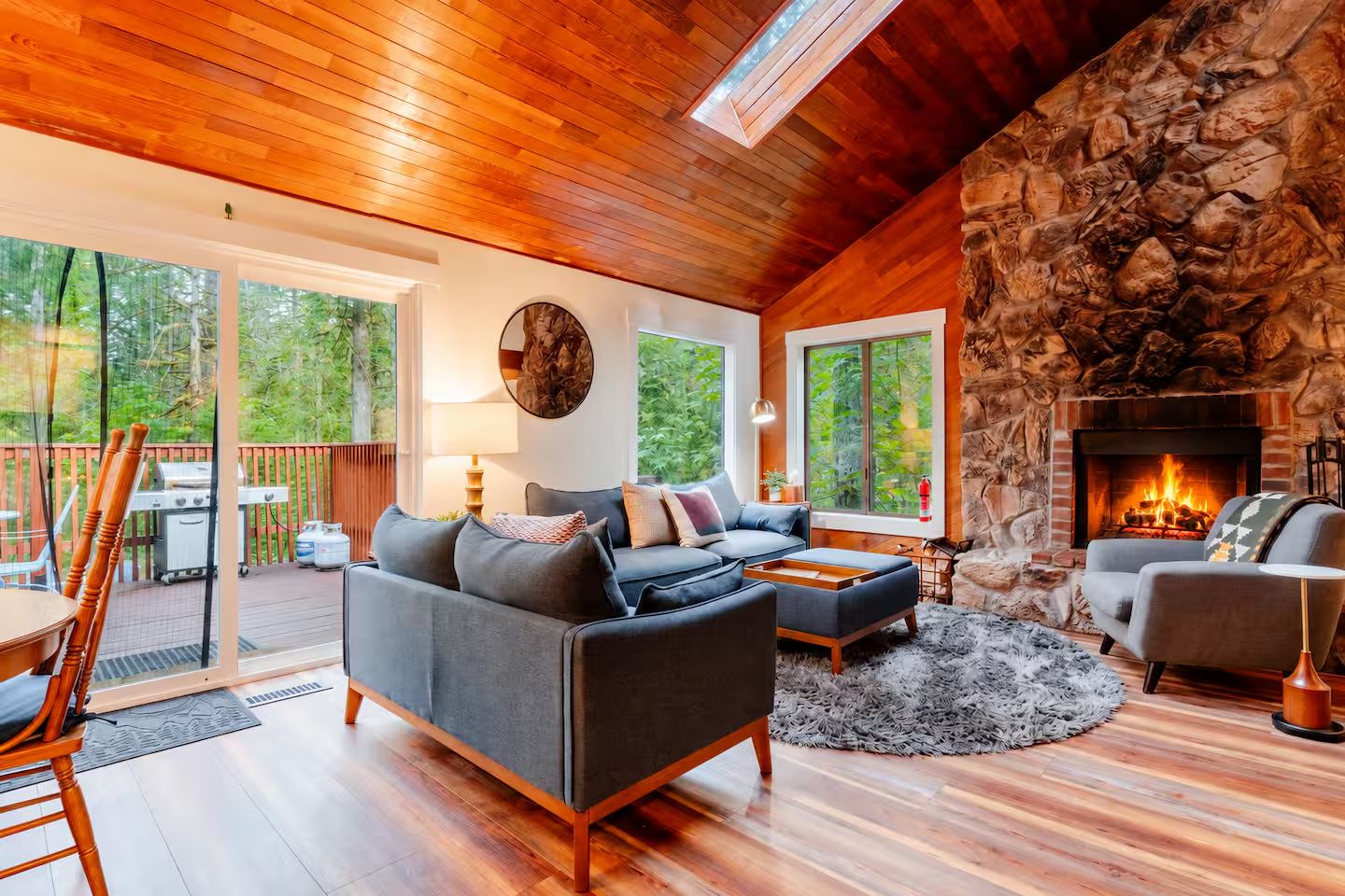 Una sala de estar acogedora con chimenea de piedra, un sofá grande y un comedor con vistas al exterior.