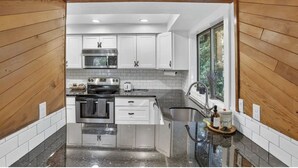 A modern kitchen with white cabinets, stainless steel appliances, and a black granite countertop.