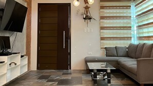 A modern living room with a sectional sofa, a glass coffee table, a TV mounted on the wall, and a ceiling light fixture. - Ranchotel Guesthouse in Villasis (Villasis)