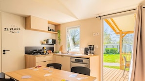 A compact kitchen with a dining area, a coffee maker, and a view of the outdoors. - Select TV LV Wi-Fi Plancha Mobile Home - 2 bedrooms - 4 people (JUGON LES LACS)