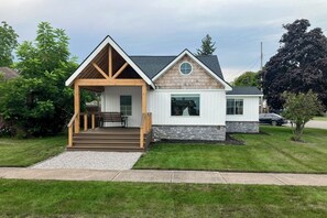 A two-story house with a covered porch, a stone foundation, and a well-maintained lawn. - Walk to Beach & Dtwn East Tawas! Lake-View Retreat (East Tawas)